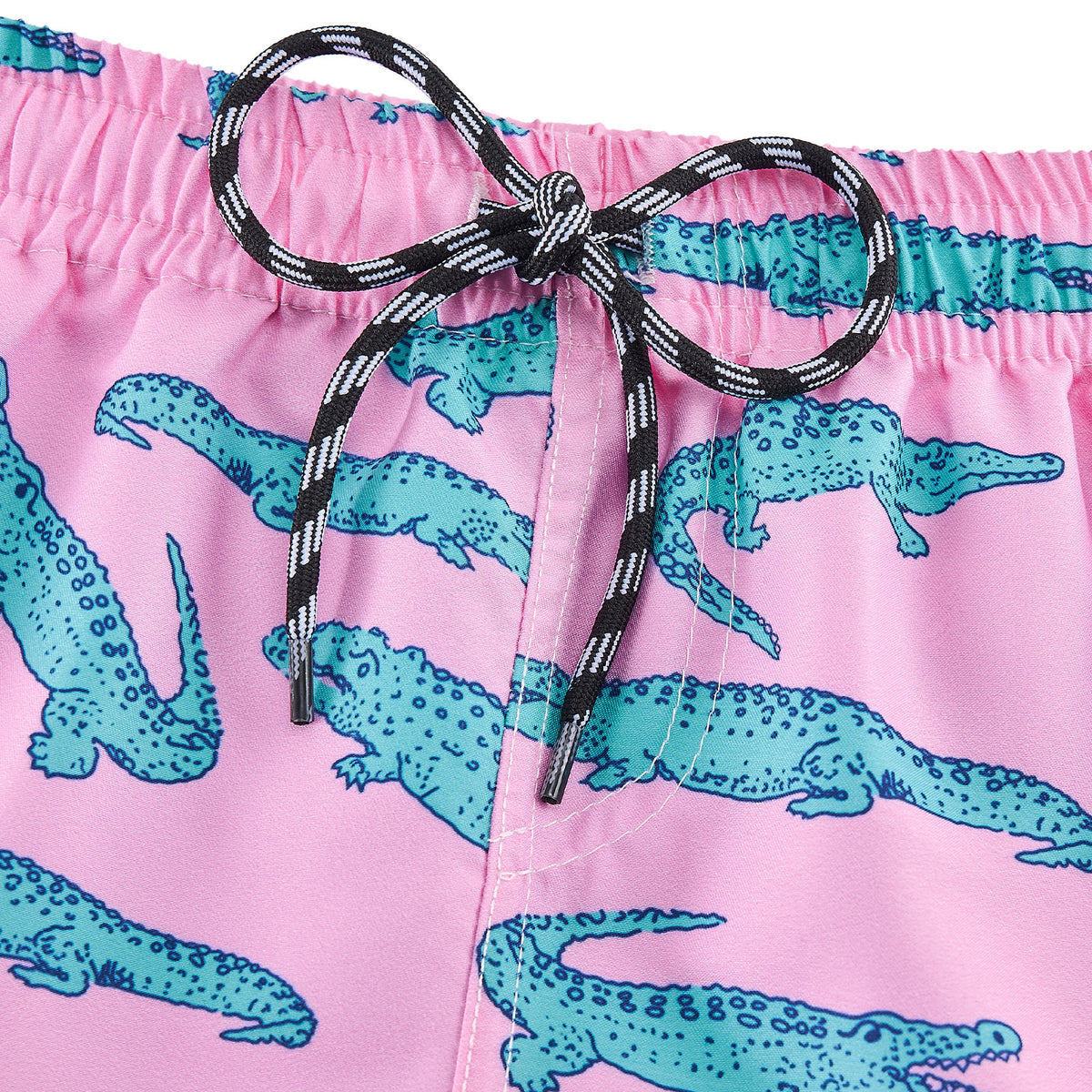 Close-up of pink crocodile print swim trunks showing the elastic waistband, black drawstring and colorful teal crocodile pattern.