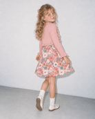 Girl wearing a Pink Daisy Floral dress with matching pink cardigan in a side standing pose, showing the layered outfit and floral skirt shape.