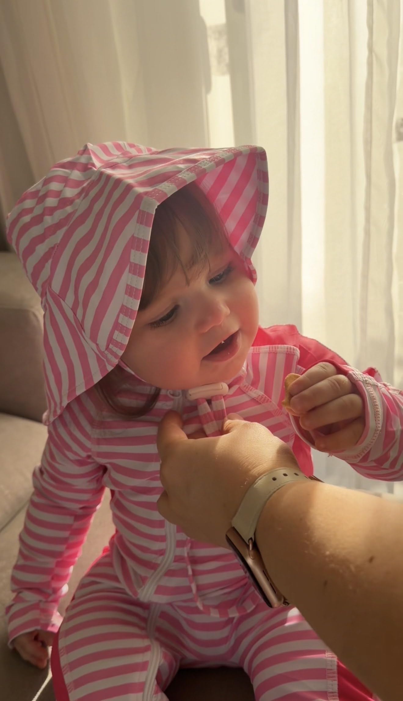 Close-up of a toddler girl wearing a pink striped rash guard swimsuit with matching sun hat, showing the full coverage swimwear fit.