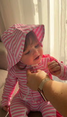 Close-up of a toddler girl wearing a pink striped rash guard swimsuit with matching sun hat, showing the full coverage swimwear fit.