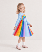 Girl wearing a rainbow tulle dress from the side, showing the flowing layered skirt and lightweight party dress silhouette.