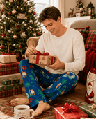 Man wearing Santa's Vacation print lounge pants while sitting beside Christmas gifts, styled for cozy holiday mornings at home.