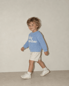 Toddler boy walking in a baby blue Big Brother sweater, showing the side fit, long sleeves and comfortable casual style.