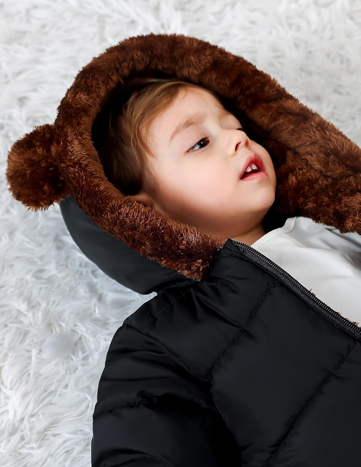 Close-up of a toddler wearing a black snowsuit with plush brown bear-ear hood, showing the cozy hood design and winter coverage.