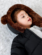Close-up of a toddler wearing a black snowsuit with plush brown bear-ear hood, showing the cozy hood design and winter coverage.