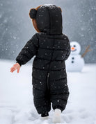 Back view of a toddler wearing a black one-piece snowsuit, showing the bear-ear hood and full-body quilted winter design.