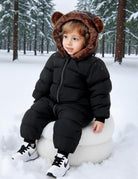 Toddler wearing a black bear ear snowsuit while sitting in the snow, showing a warm one-piece winter outfit for outdoor play.