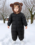Toddler standing in the snow wearing a black bear ear hooded snowsuit, showing the full-body fit for cold-weather outdoor activities.