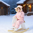 Toddler wearing a pink bear ear puffer snowsuit while sitting on a sled in the snow, styled for playful winter outdoor adventures.
