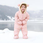 Toddler standing in the snow wearing a pink bear ear puffer snowsuit, showing the warm one-piece fit for winter outdoor activities.