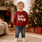 Toddler wearing a wine red Santa Baby sweater beside Christmas decorations, styled for a festive holiday outfit and family photos.